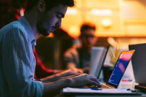 Male entrepreneur working late in office. He is sitting, using his laptop to try to solve problem with code.