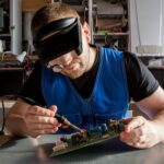 Engineer soldering a circuit board while wearing magnifying safety glasses