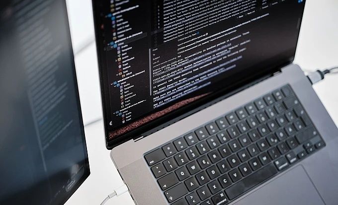 Laptop displaying open-source code beside a second monitor